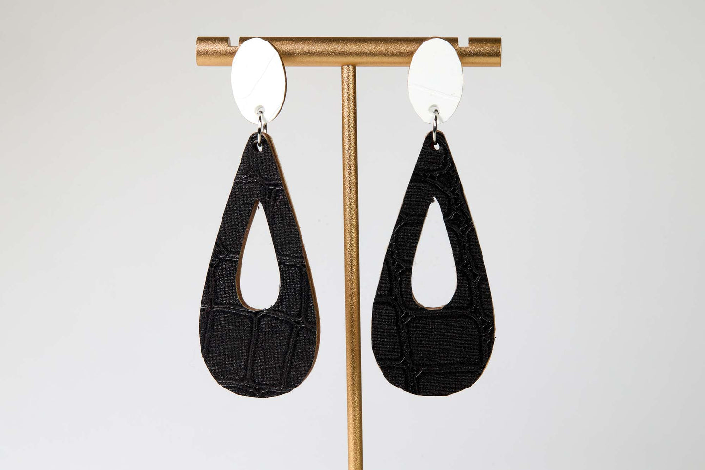 Black teardrop earrings on a gold earring stand against a white background