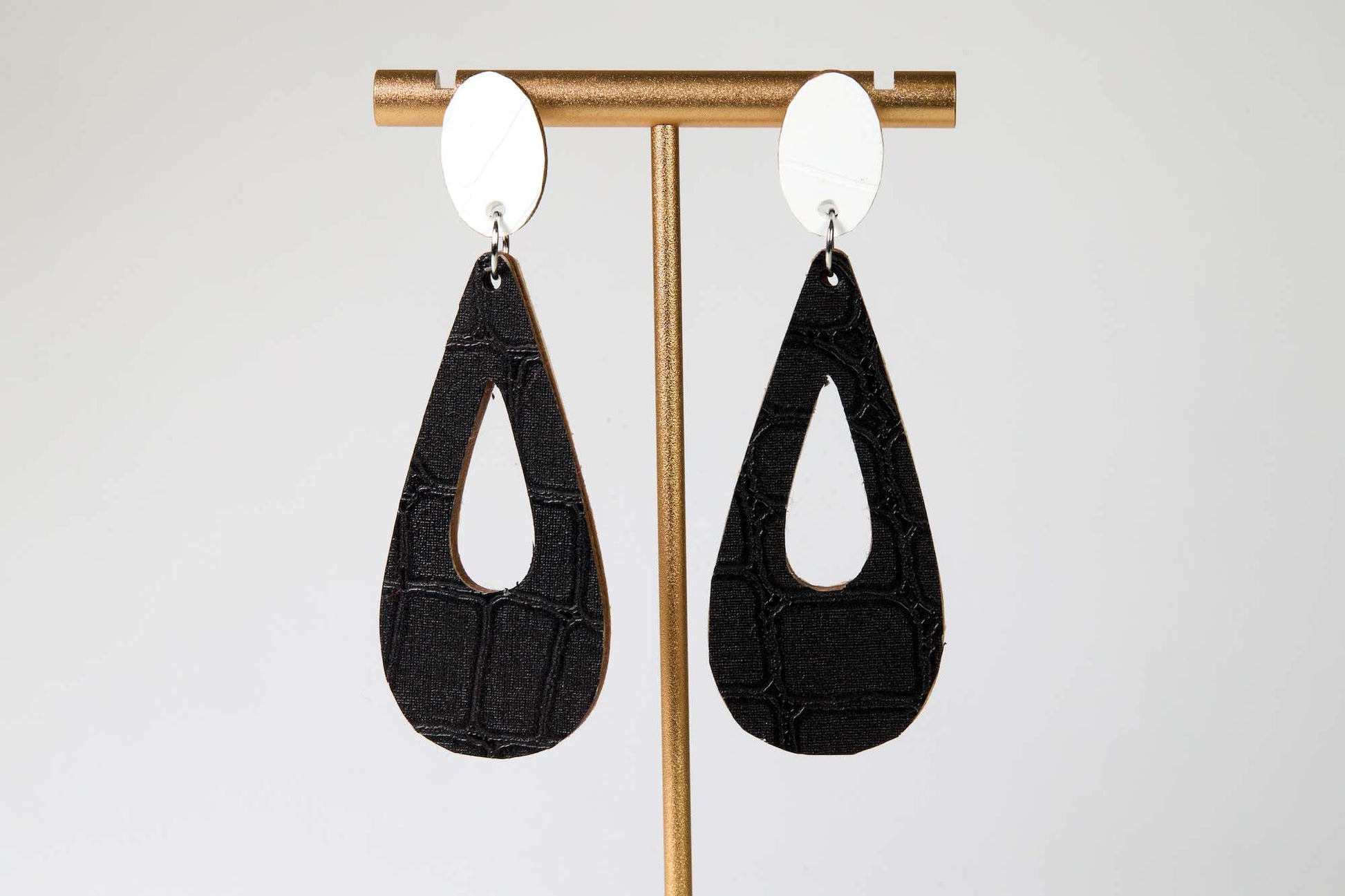 Black teardrop earrings on a gold earring stand against a white background