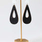 Black teardrop-shaped earrings on a gold earring stand against a white background