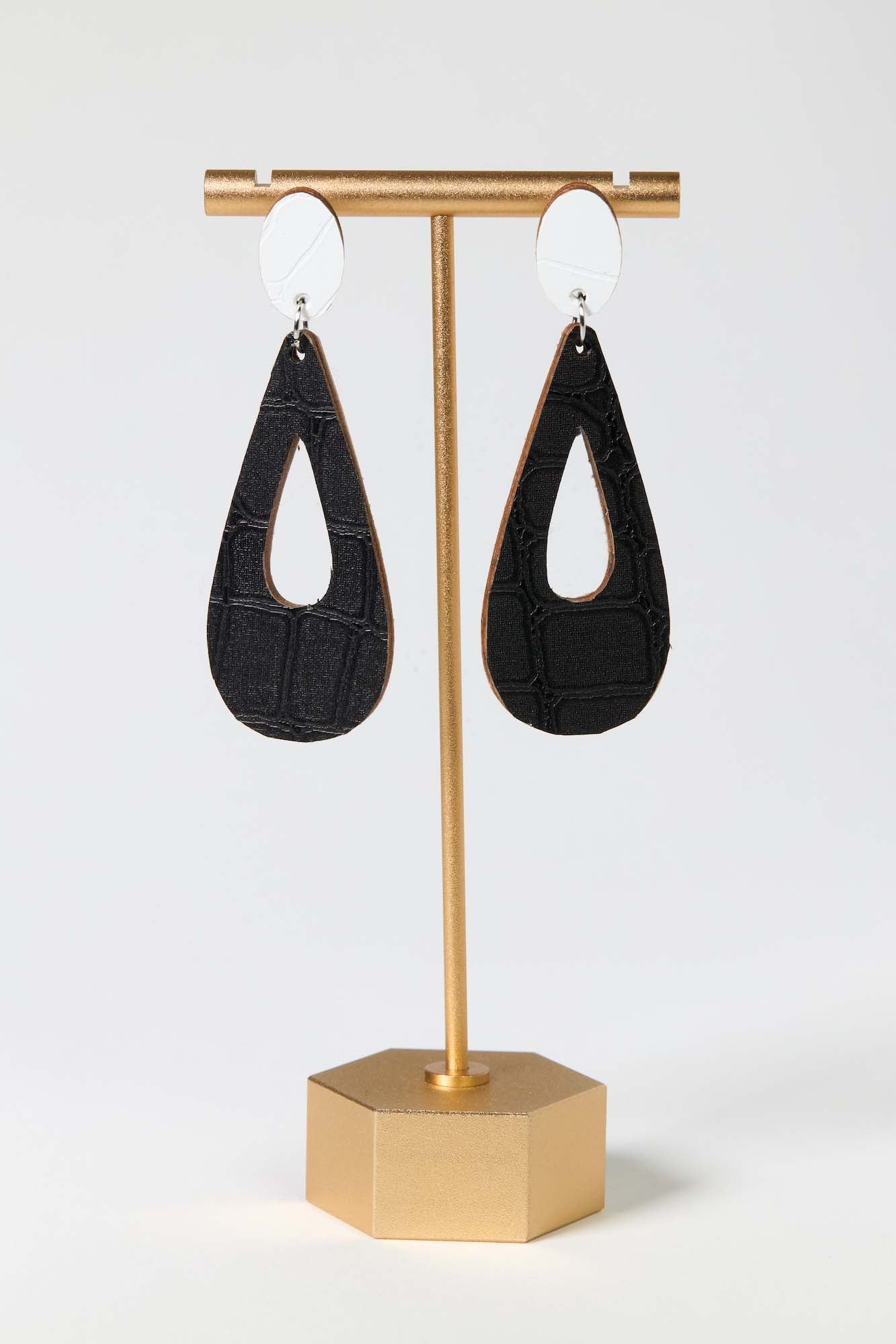 Black teardrop-shaped earrings on a gold earring stand against a white background