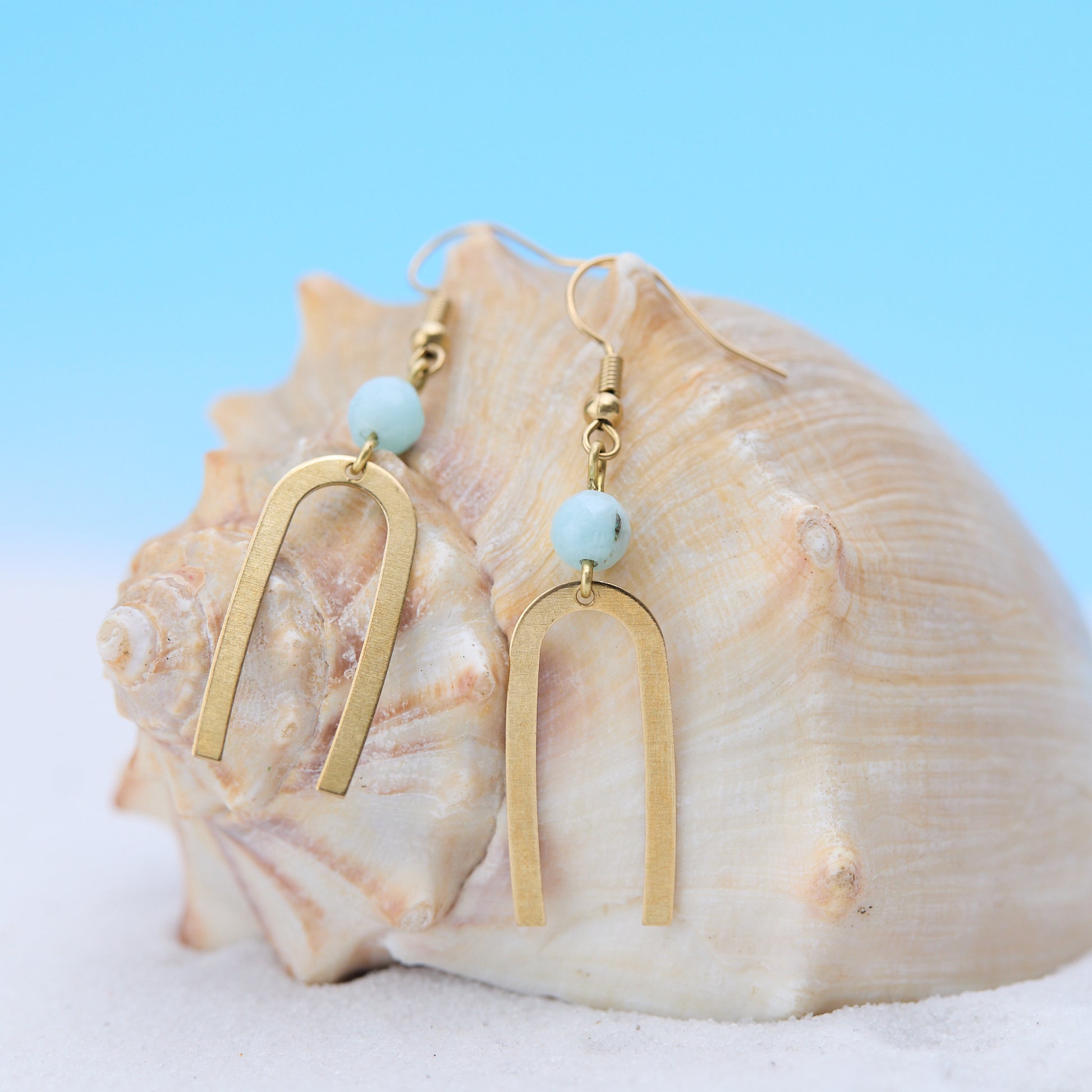 Gold earrings with turquoise beads on a seashell against a blue background