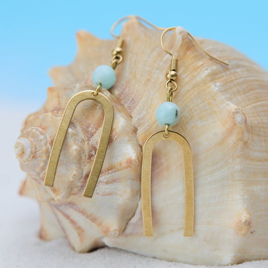 Gold earrings with turquoise beads on a seashell against a blue background