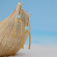 Gold earrings with turquoise beads on a wooden surface with a blue gradient background