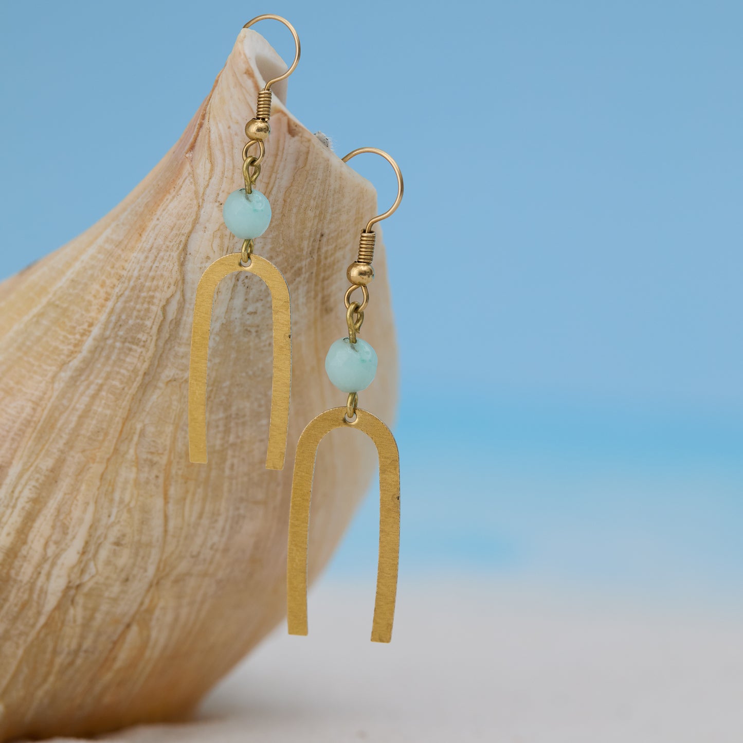 Gold earrings with turquoise beads on a wooden surface with a blue gradient background