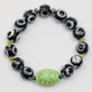 Black and white beaded bracelet with a green carved bead on a white background