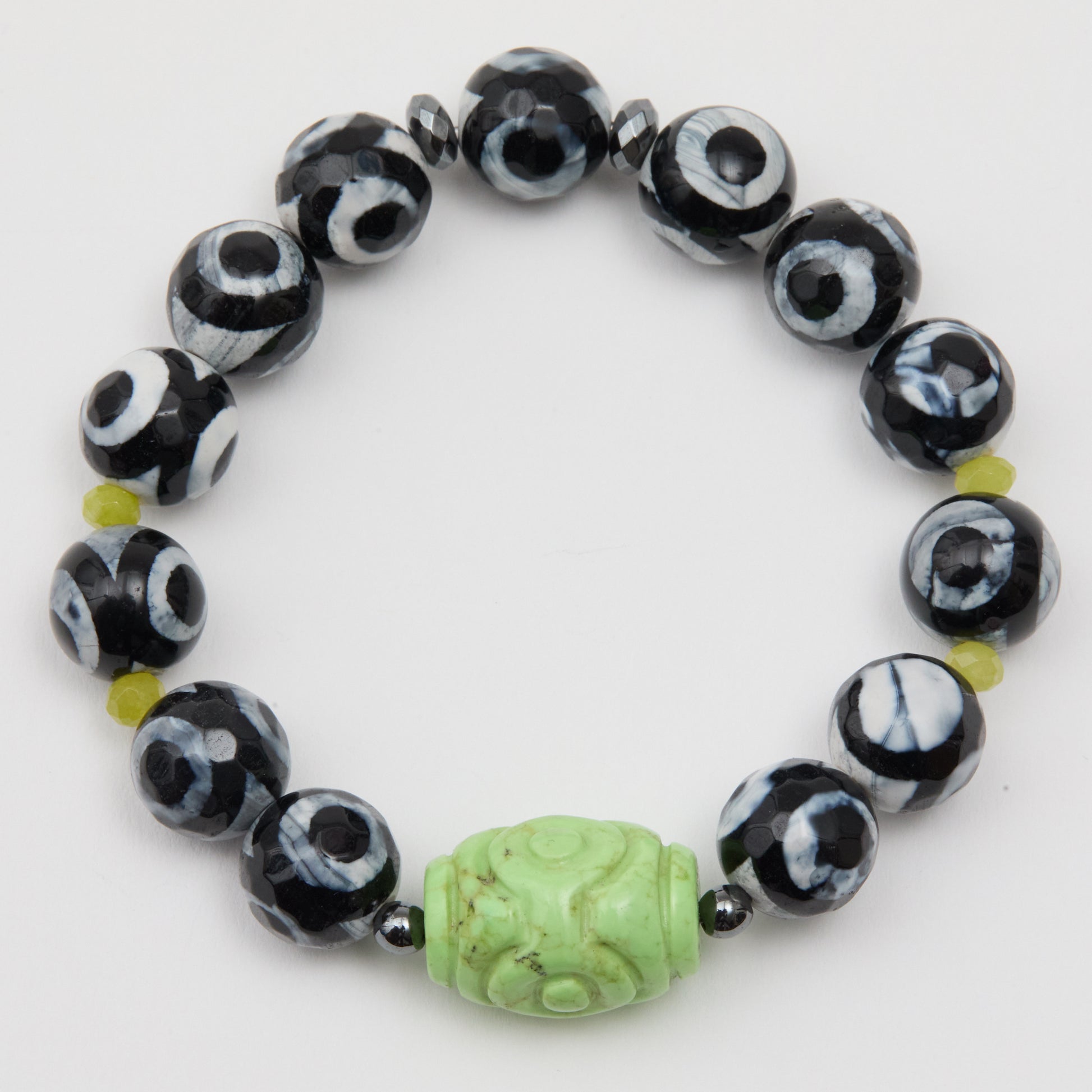 Black and white beaded bracelet with a green carved bead on a white background