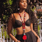 Woman wearing a black bra and skirt with a long beaded necklace outdoors.