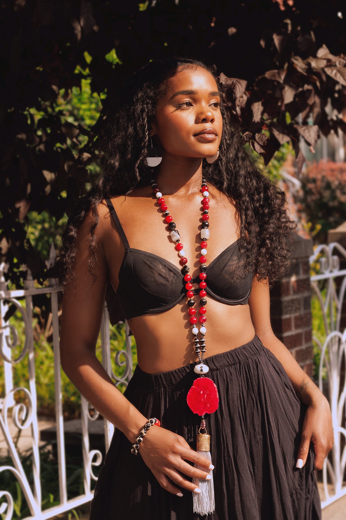 Woman wearing a black bra and skirt with a long beaded necklace outdoors.