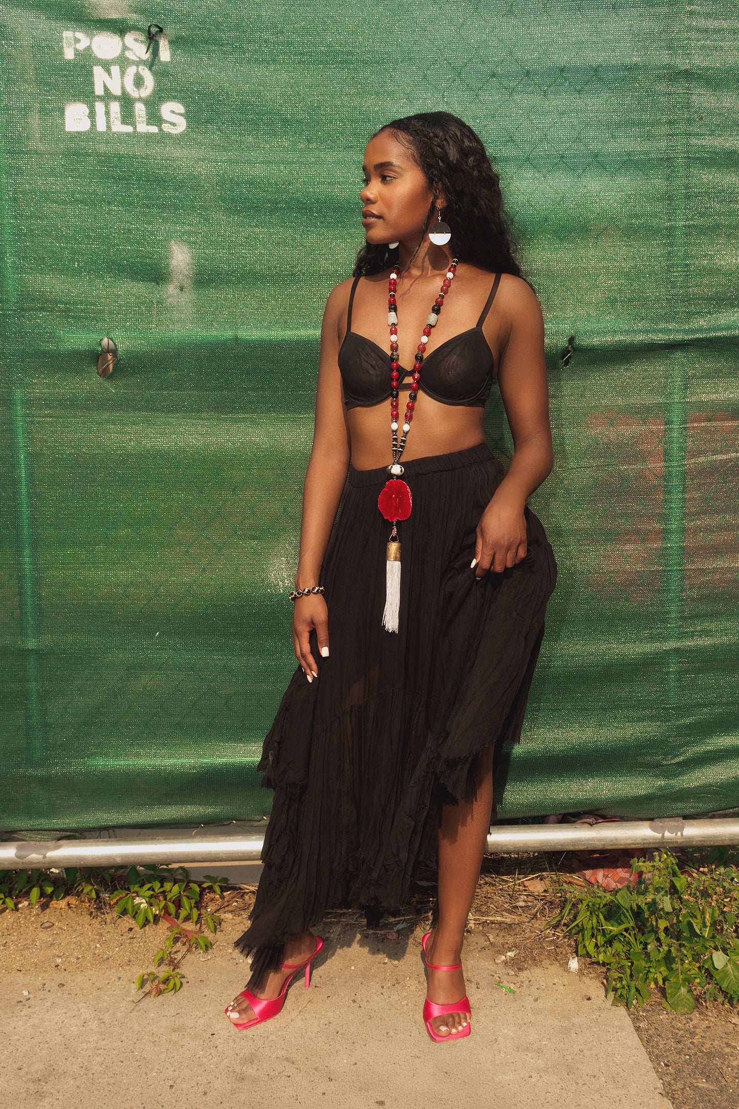 Woman in black outfit with pink sandals standing against a green tarp.
