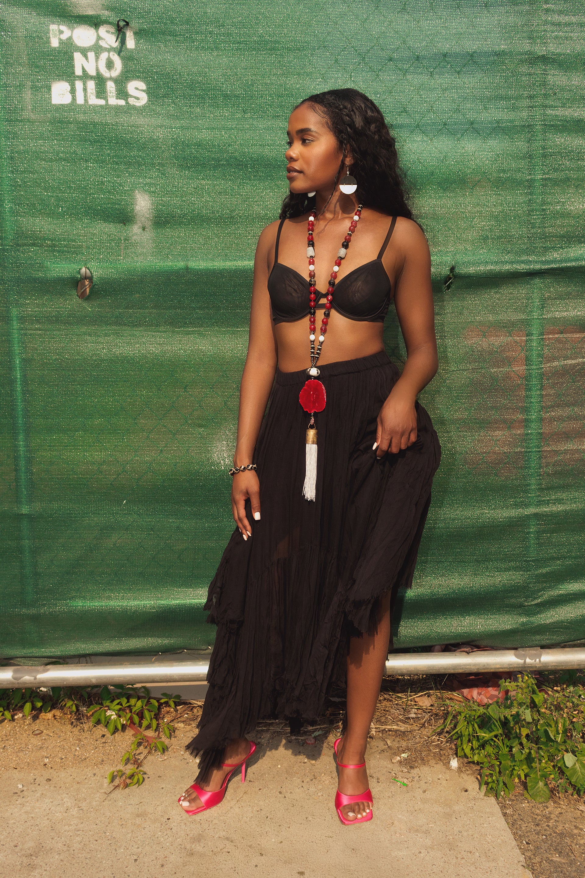 Woman in black outfit with pink sandals standing against a green tarp.