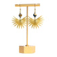 A pair of earrings featuring brass sun spikes and tiger eye coin beads displayed on a gold-colored stand against white background.