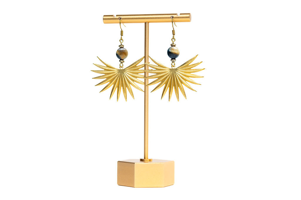 A pair of earrings featuring brass sun spikes and tiger eye coin beads displayed on a gold-colored stand against white background.