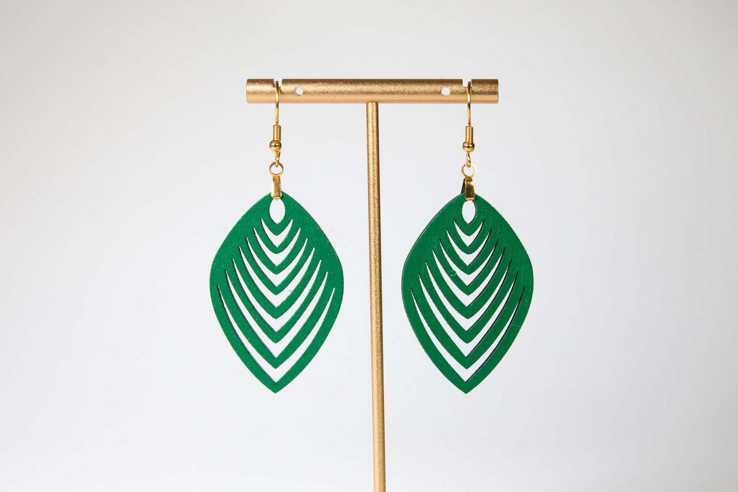 Green leaf-shaped earrings on a gold earring stand against a white background