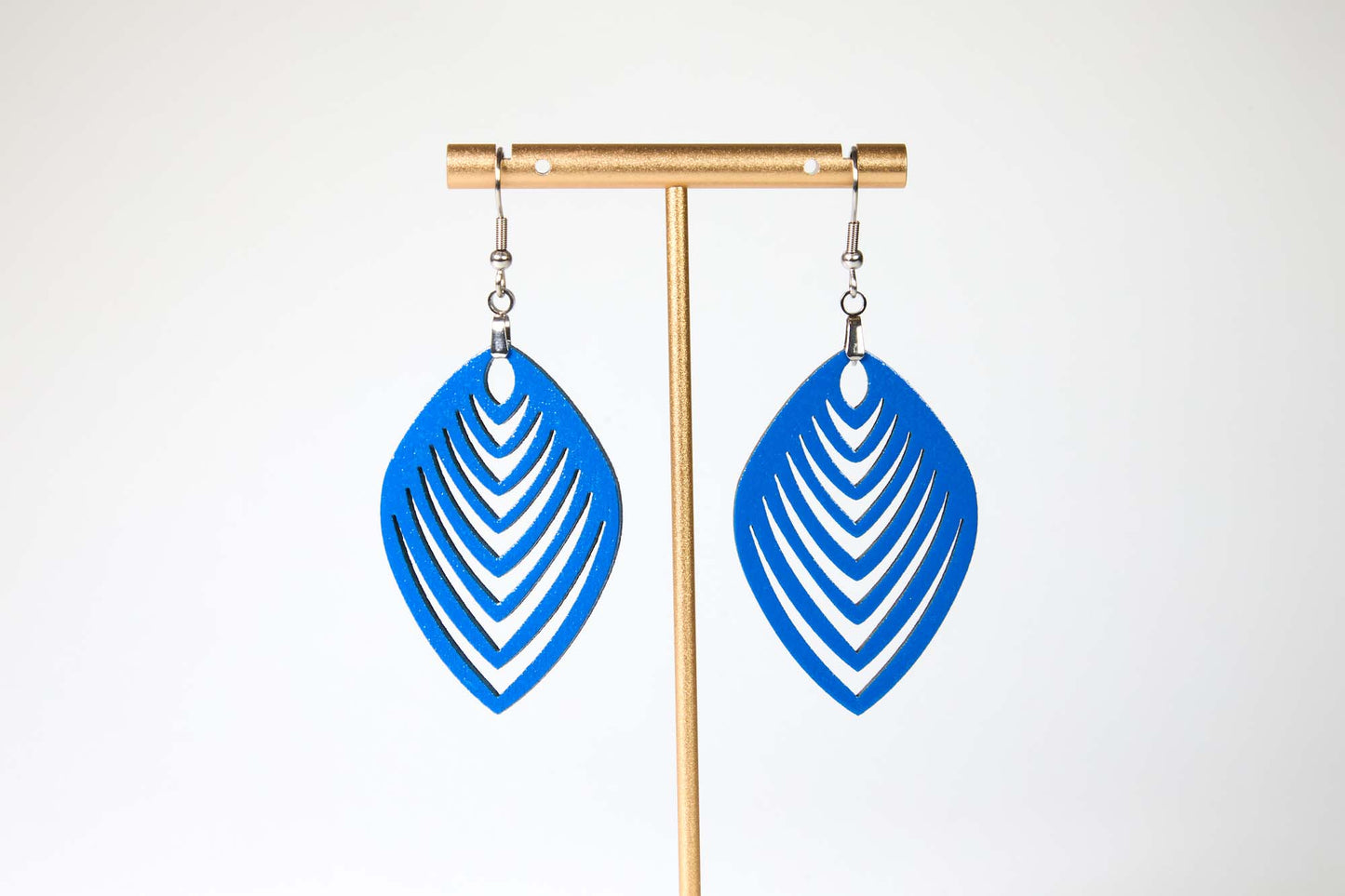 Blue leaf-shaped earrings on a gold earring stand against a white background