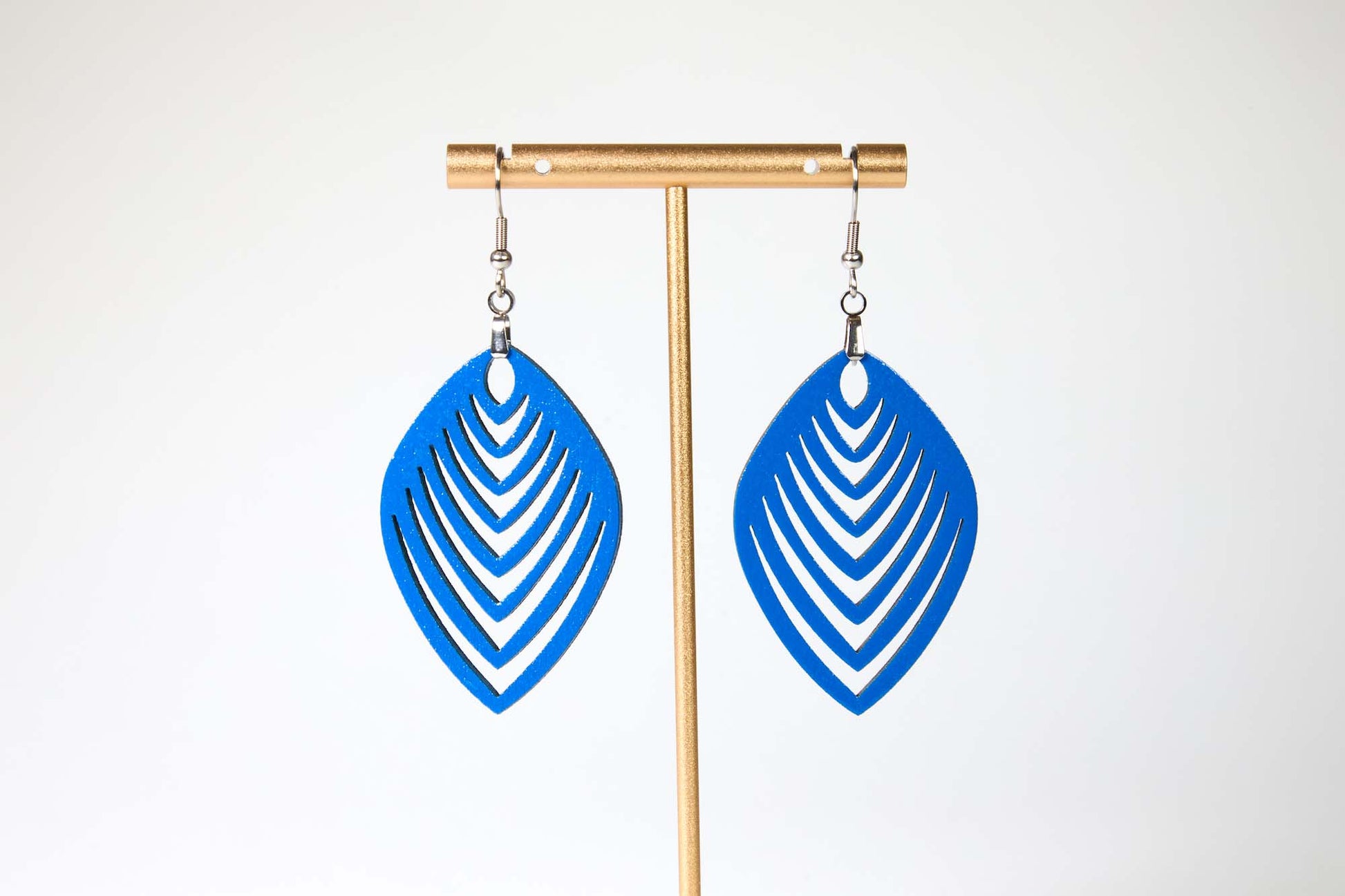 Blue leaf-shaped earrings on a gold earring stand against a white background