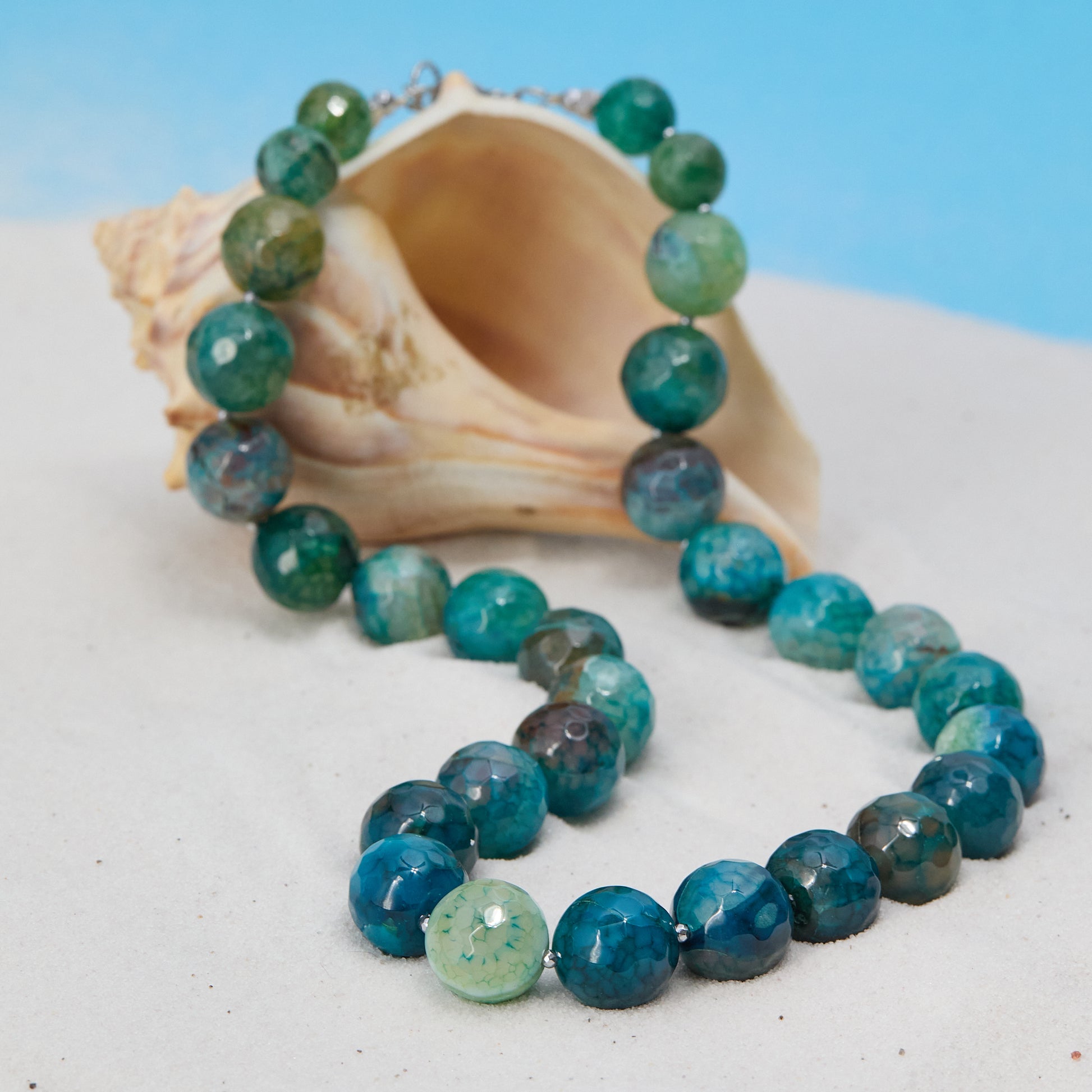Necklace with blue and green beads on a shell against a blue background