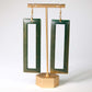 Green open rectangular earrings on a gold stand against a white background
