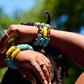 Close-up of hands with colorful blue and yellow beaded bracelets against a blurred natural background