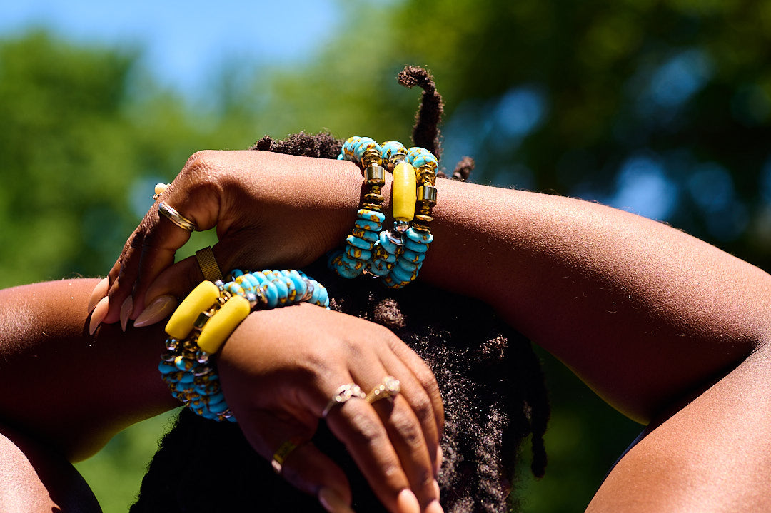Close-up of hands with colorful blue and yellow beaded bracelets against a blurred natural background